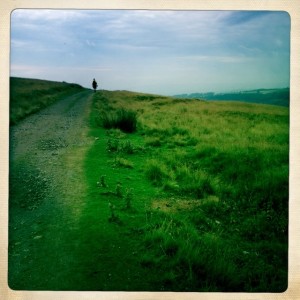 Road across moor land with farms on the valley to our right.